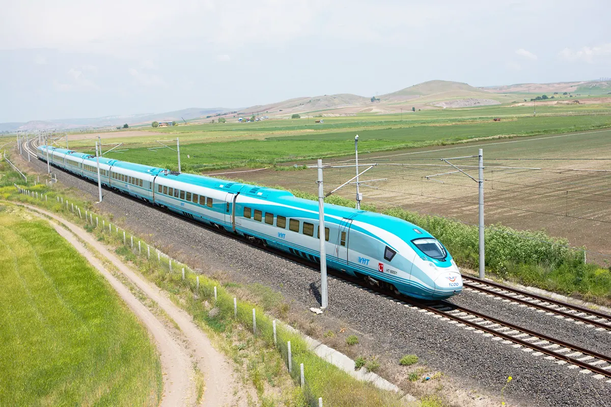 A high-speed train crosses a green plain in Turkey