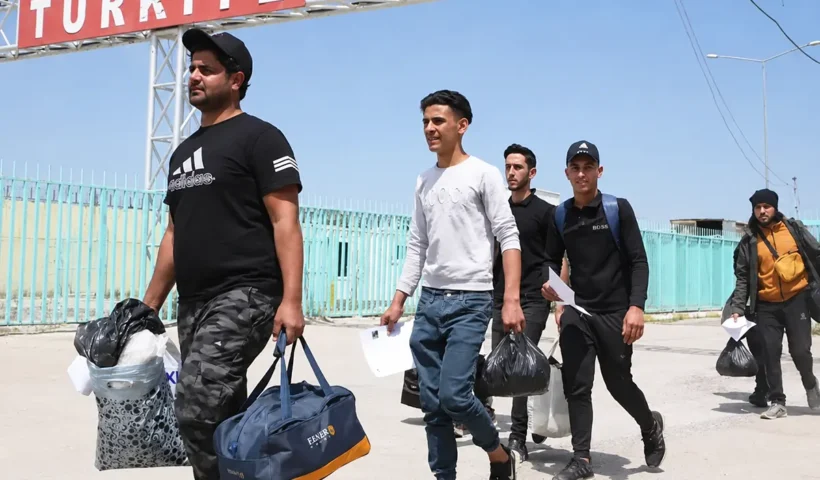 un grupo de inmigrantes atraviesa la frontera cargado con bolsas bajo un cartel que pone "Türkiye"