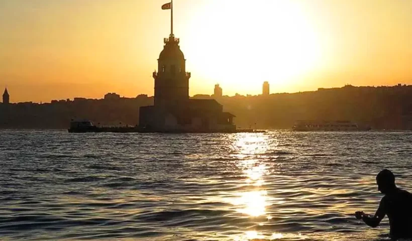a person in the waters of the Bosphorus next to the Maiden’s Tower in Istanbul, with the city skyline in the background, in an image with ochre tones