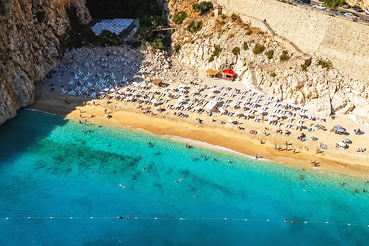 An aerial view of Kaputaş Beach in Antalya, set on a narrow cliff and facing a sea of turquoise waters, teeming with people
