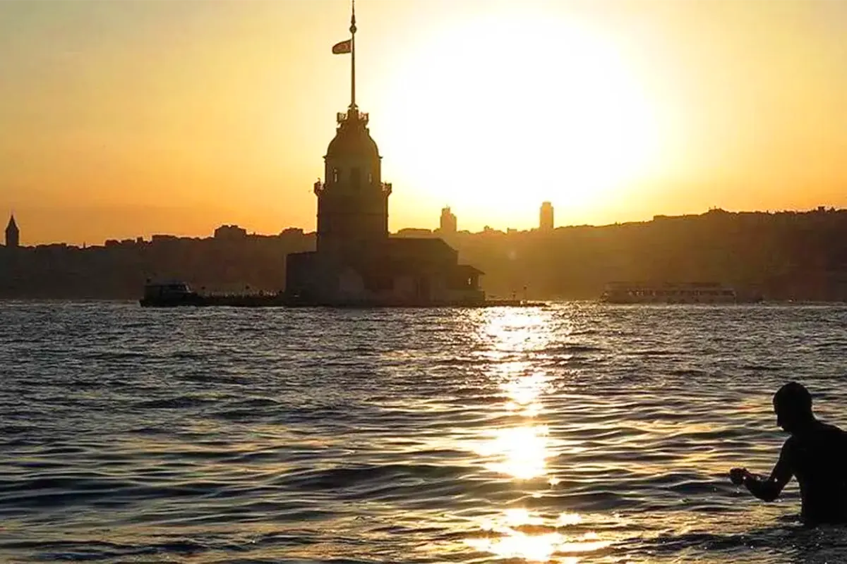 una persona en el agua del Bósforo junto a la Torre de la Doncella en Estambul, con la silueta de la ciudad de fondo en una imagen con colores ocres