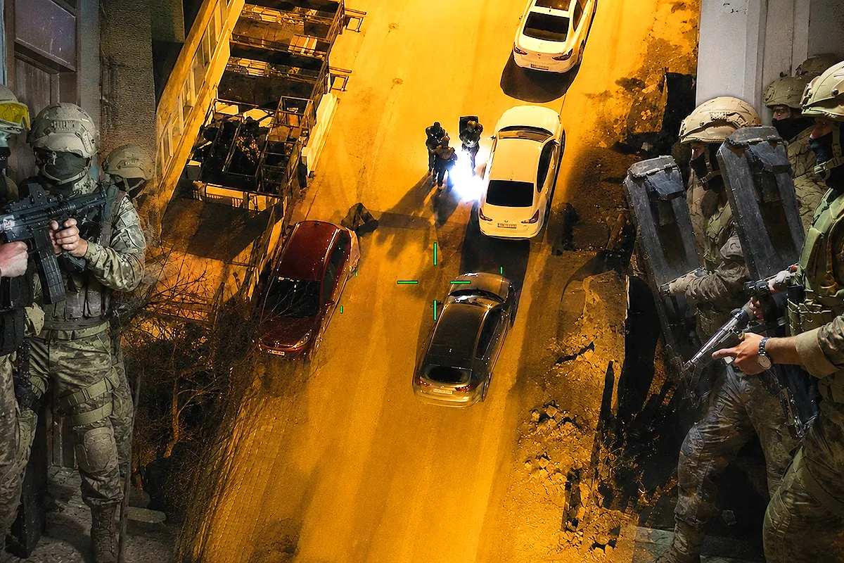 una imagen aérea nocturna de un dron mostrando a varios policías armados avanzando por una calle; a los laterales, miembros de las fuerzas especiales de la policía y la gendarmería turcas