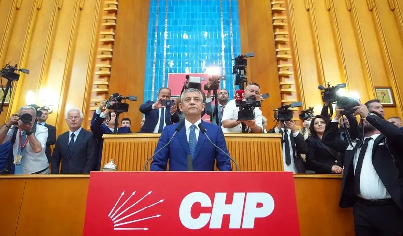 Özgür Özel subido a un podio sobre el que hay un gran cartel rojo con las siglas del partido CHP, rodeado de periodistas