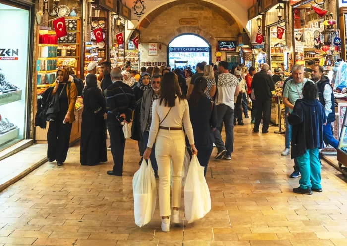 A woman in the foreground carrying shopping bags as she walks through the Egyptian Bazaar in Istanbul, which is filled with shops and people