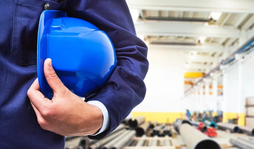 un trabajador sujetando un casco bajo su brazo en una fábrica
