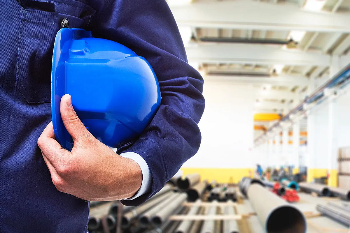 un trabajador sujetando un casco bajo su brazo en una fábrica