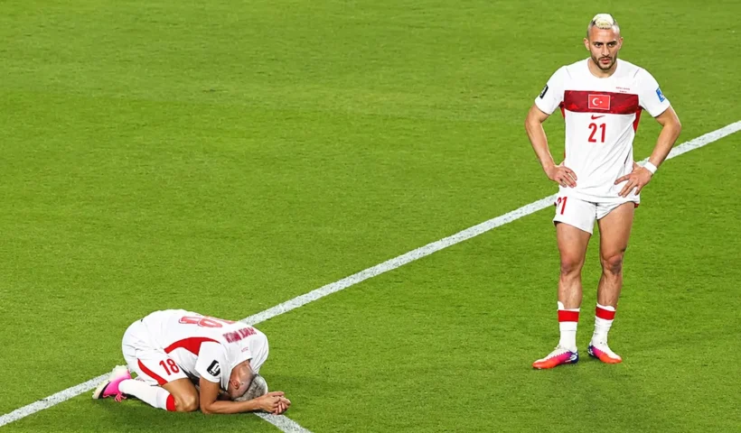 a Turkish player standing on the pitch looking stunned, and another beside him on his knees with his face pressed against the grass, crying