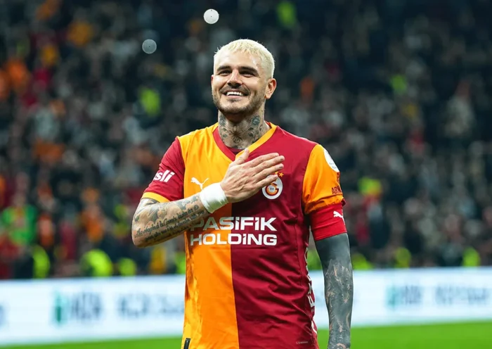 a picture of a smiling Mauro Icardi wearing a Galatasaray shirt and placing his hand on his chest in the middle of a stadium