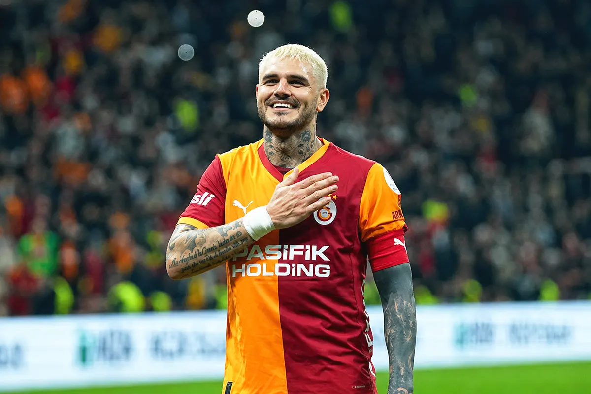 a picture of a smiling Mauro Icardi wearing a Galatasaray shirt and placing his hand on his chest in the middle of a stadium