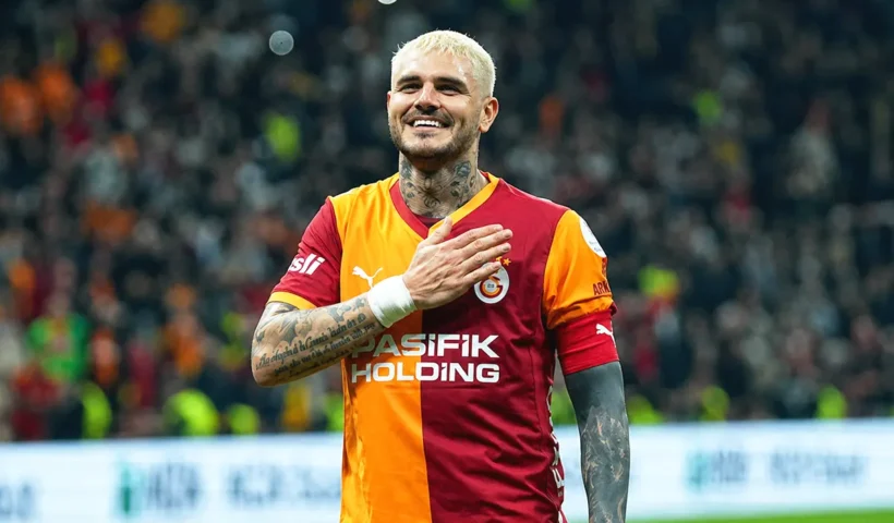 una imagen de Mauro Icardi sonriente vistiendo la camiseta del Galatasaray y llevándose la mano al pecho en medio de un estadio
