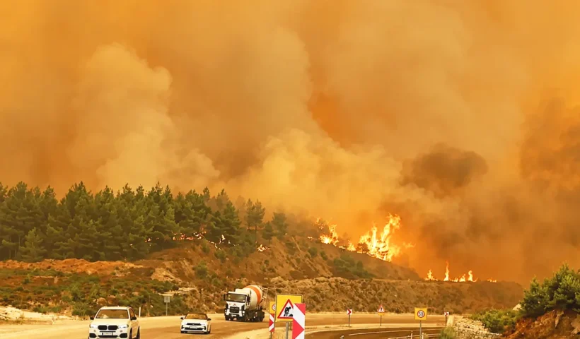 several vehicles travelling along a motorway next to a burning hill and surrounded by smoke, set against an orange, almost apocalyptic backdrop