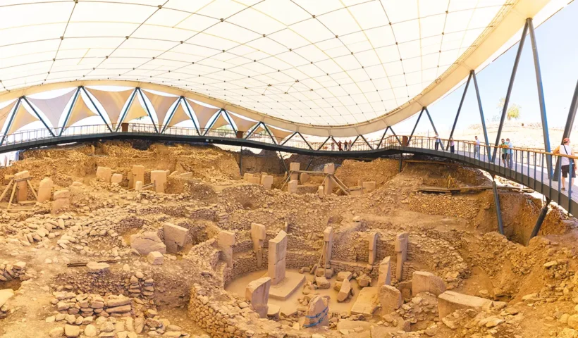 several stone pillars and stone circles at the Göbeklitepe sanctuary, viewed by tourists