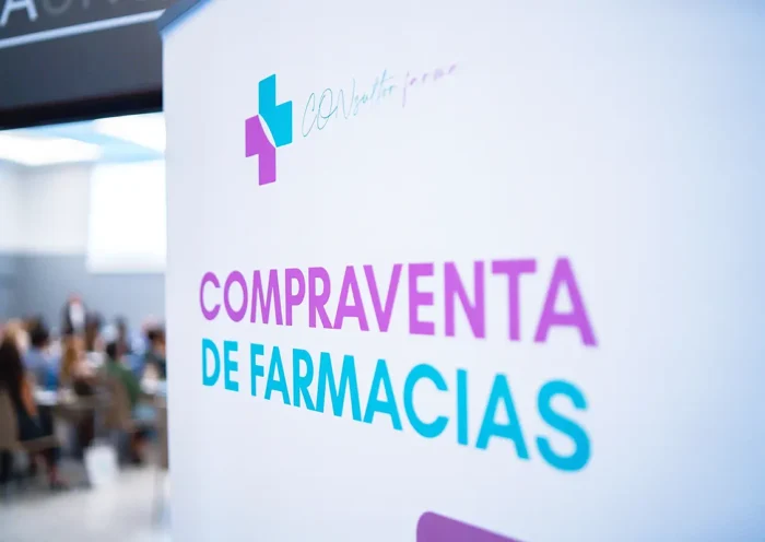 un cartel junto a un evento con público reza "compraventa de farmacias"