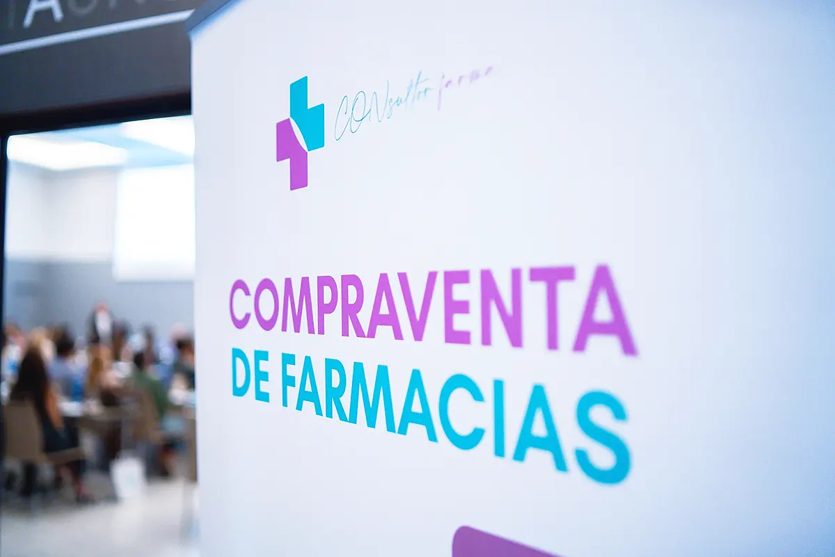 un cartel junto a un evento con público reza "compraventa de farmacias"