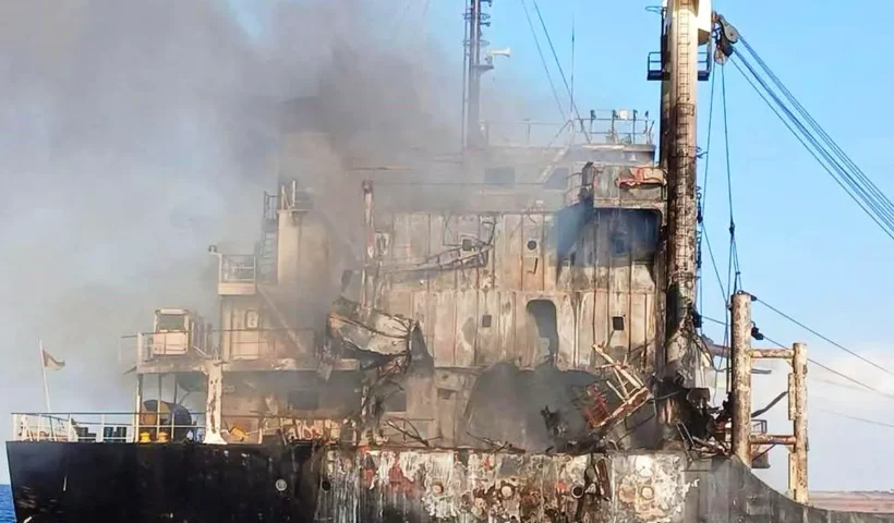 a cargo ship billowing smoke and showing signs of impact and fire damage to its structure