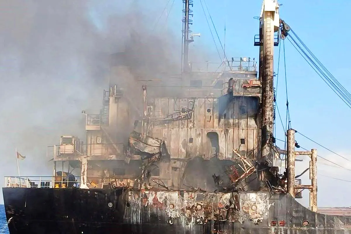 a cargo ship billowing smoke and showing signs of impact and fire damage to its structure
