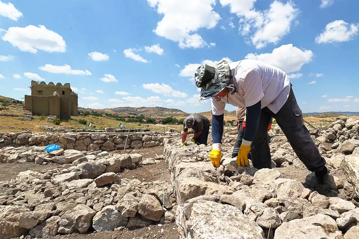 Archaeologists in the foreground working on the remains of buildings, with the restored walls of Hattusa in the background