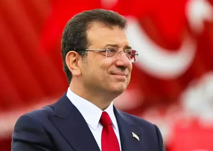 a picture of İmamoğlu wearing a suit and tie and smiling against a red background