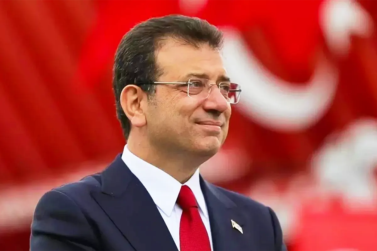 una imagen de İmamoğlu vistiendo traje y corbata y sonriendo sobre un fondo rojo