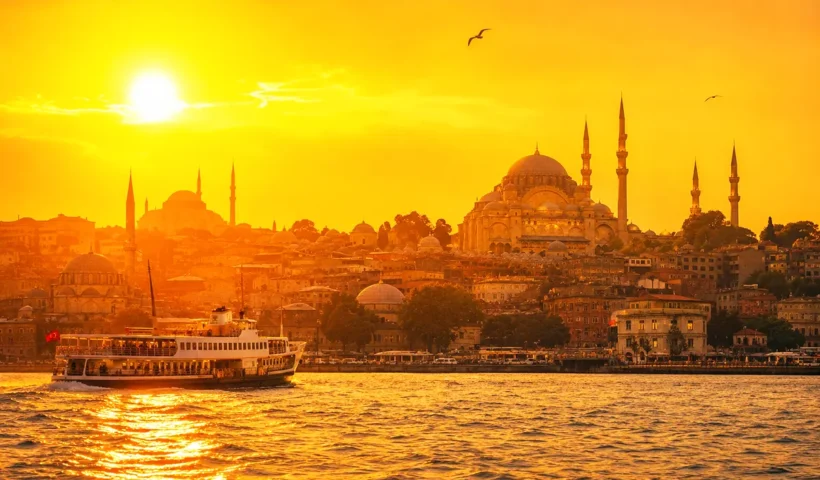 una imagen de varios edificios de Estambul a orillas del Cuerno de Oro durante el atardecer, con tonos anaranjados y ocres, en medio de un día caluroso