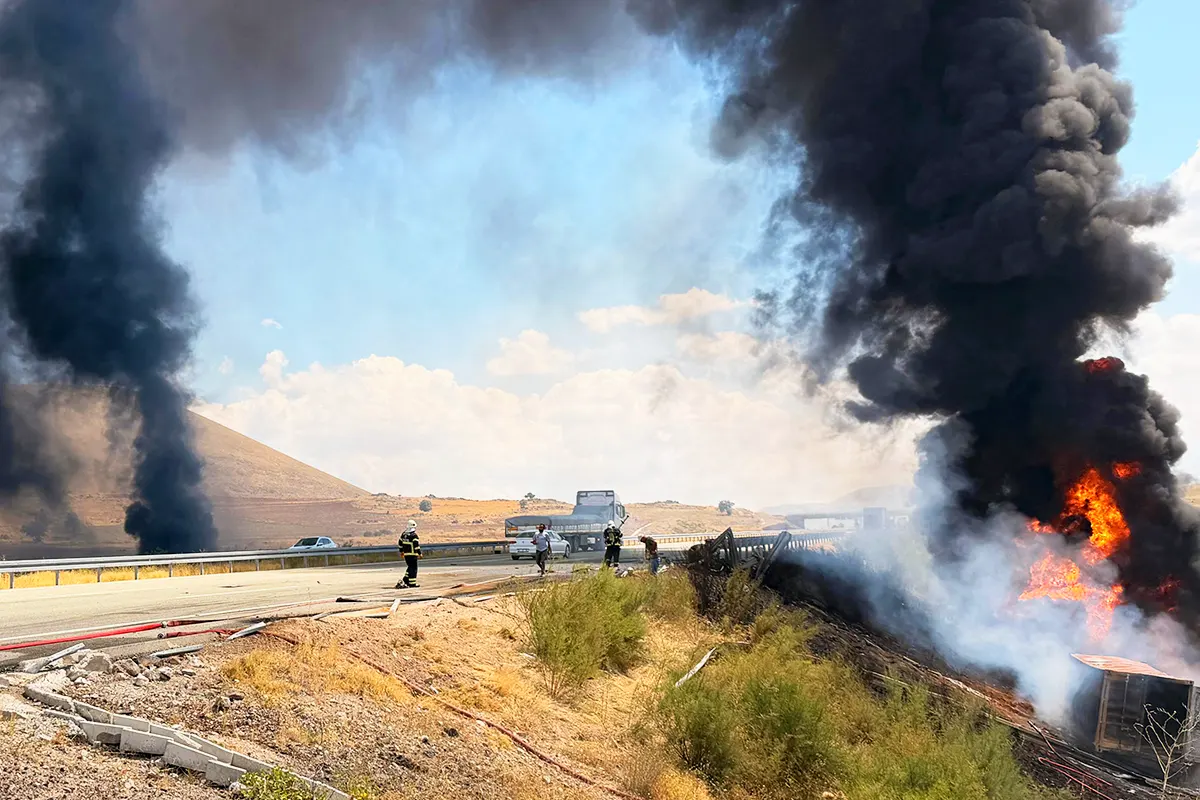 Several firefighters standing beside a motorway and a burning lorry amidst huge plumes of smoke