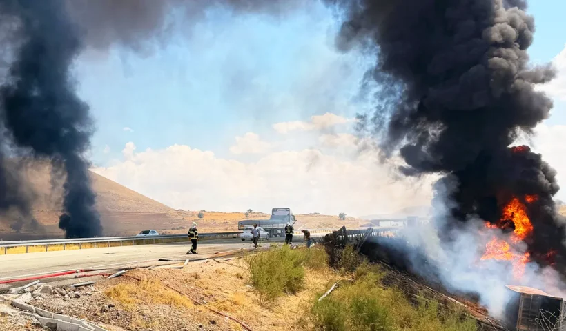 varios bomberos junto a una autopista y un camión ardiendo en medio de grandes columnas de humo