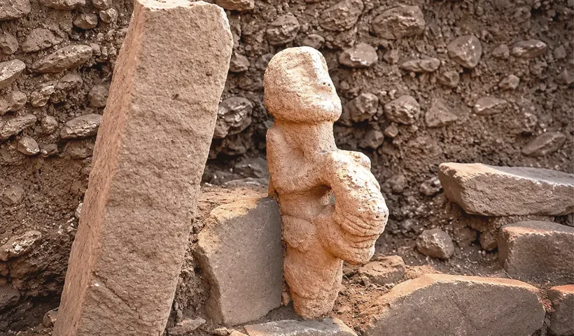 estatua de piedra con forma humana junto a unas piedras en un yacimiento arqueológico