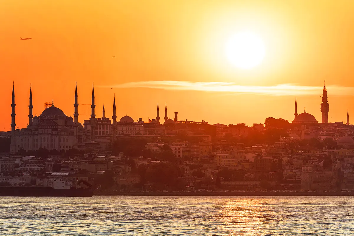 the silhouette of Istanbul from the Bosphorus, bathed in golden hues, with the sun high in the sky