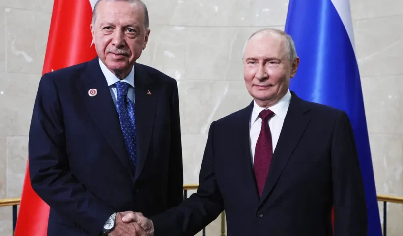 Erdoğan and Putin smile and shake hands as they pose for the photographers against a backdrop of the Turkish and Russian flags