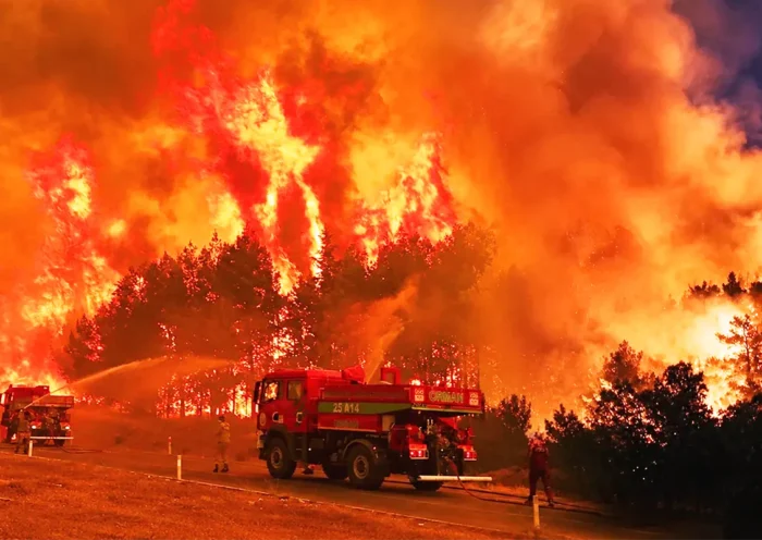 bomberos luchando contra un inmenso fuego que quema un bosque, con llamas que alcanzan más de 10 metros de altura