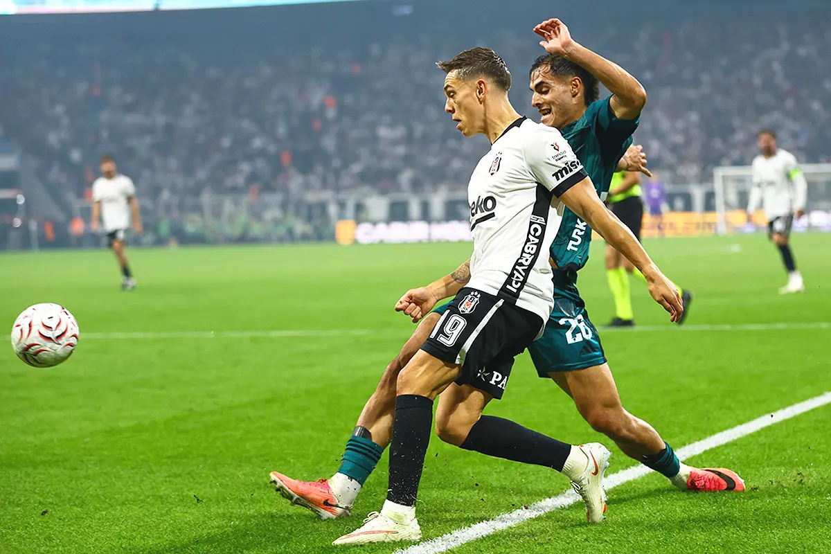 A Beşiktaş player and a Kocaelispor player battling for the ball by the touchline in a packed stadium at night
