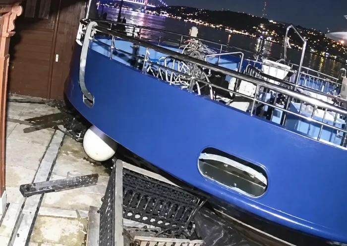 la proa de un barco de color azul chocando y subiéndose a un muelle en plena noche
