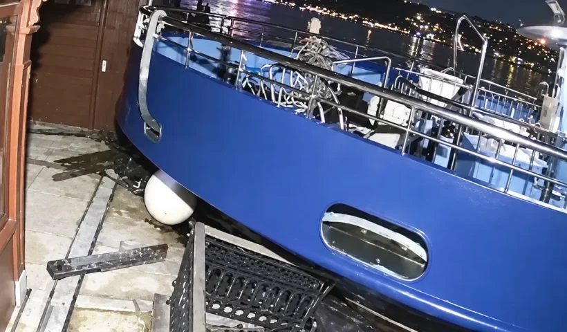 la proa de un barco de color azul chocando y subiéndose a un muelle en plena noche