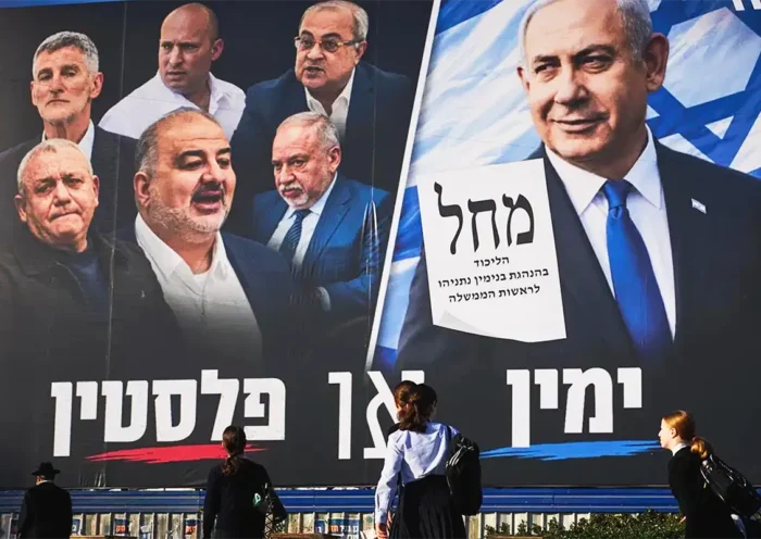 varias personas caminan junto a un cartel electoral que muestra a Netanyahu mirando desafiante a políticos de la oposición y de la minoría árabe