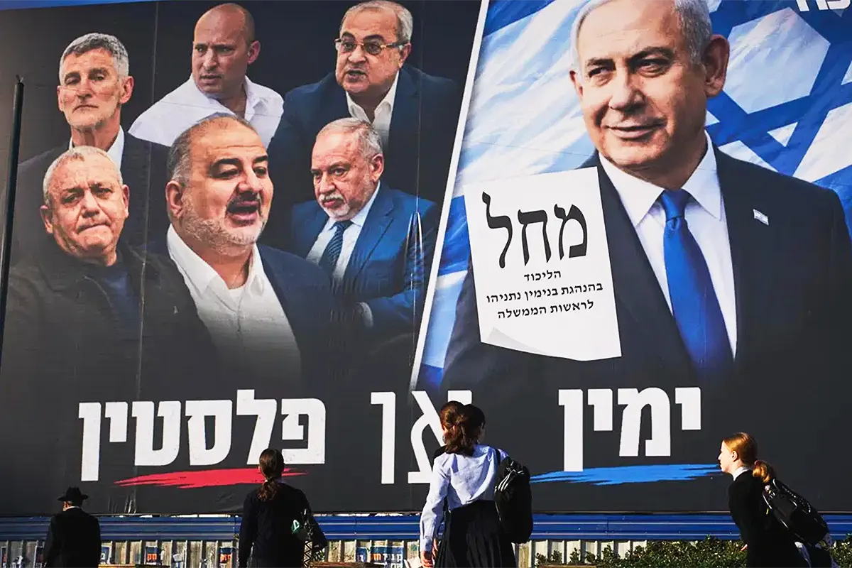 Several people are walking past an election poster showing Netanyahu glaring defiantly at opposition politicians and members of the Arab minority