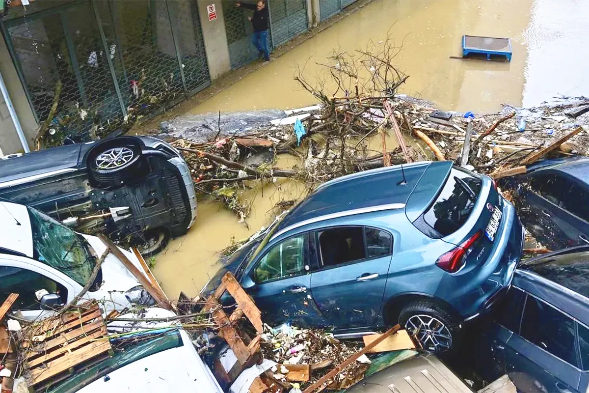 several cars piled up on a flooded street alongside rubble and debris swept away by a flash flood