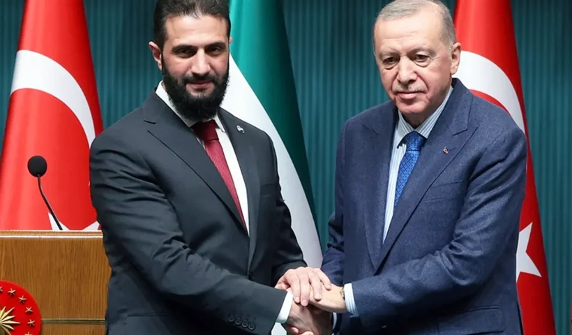 una imagen de Al-Sharaa estrechando sus manos con Erdoğan con las banderas de Turquía y Siria de fondo